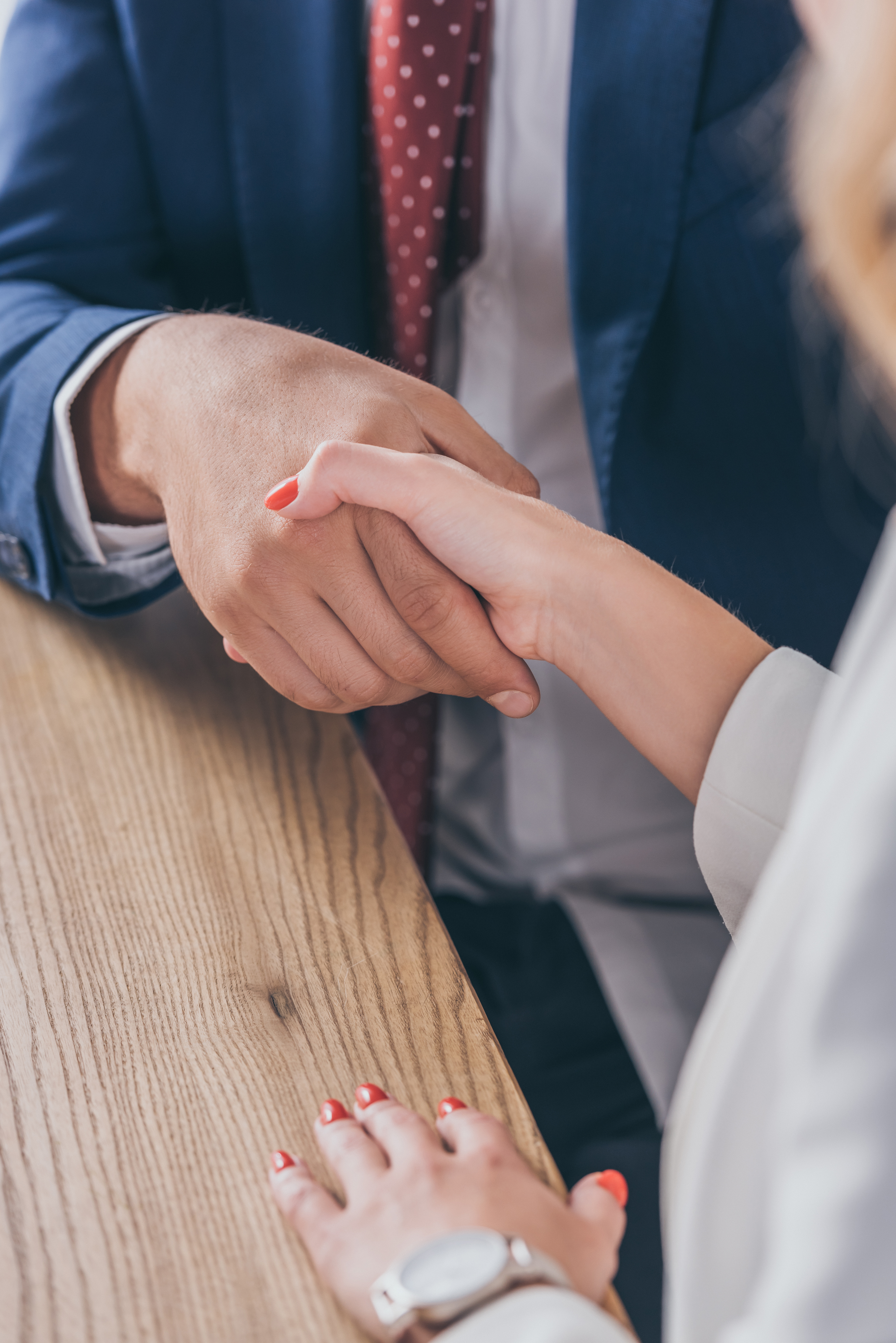 cropped view of businessman shaking hands with woman while sitting at wooden desk