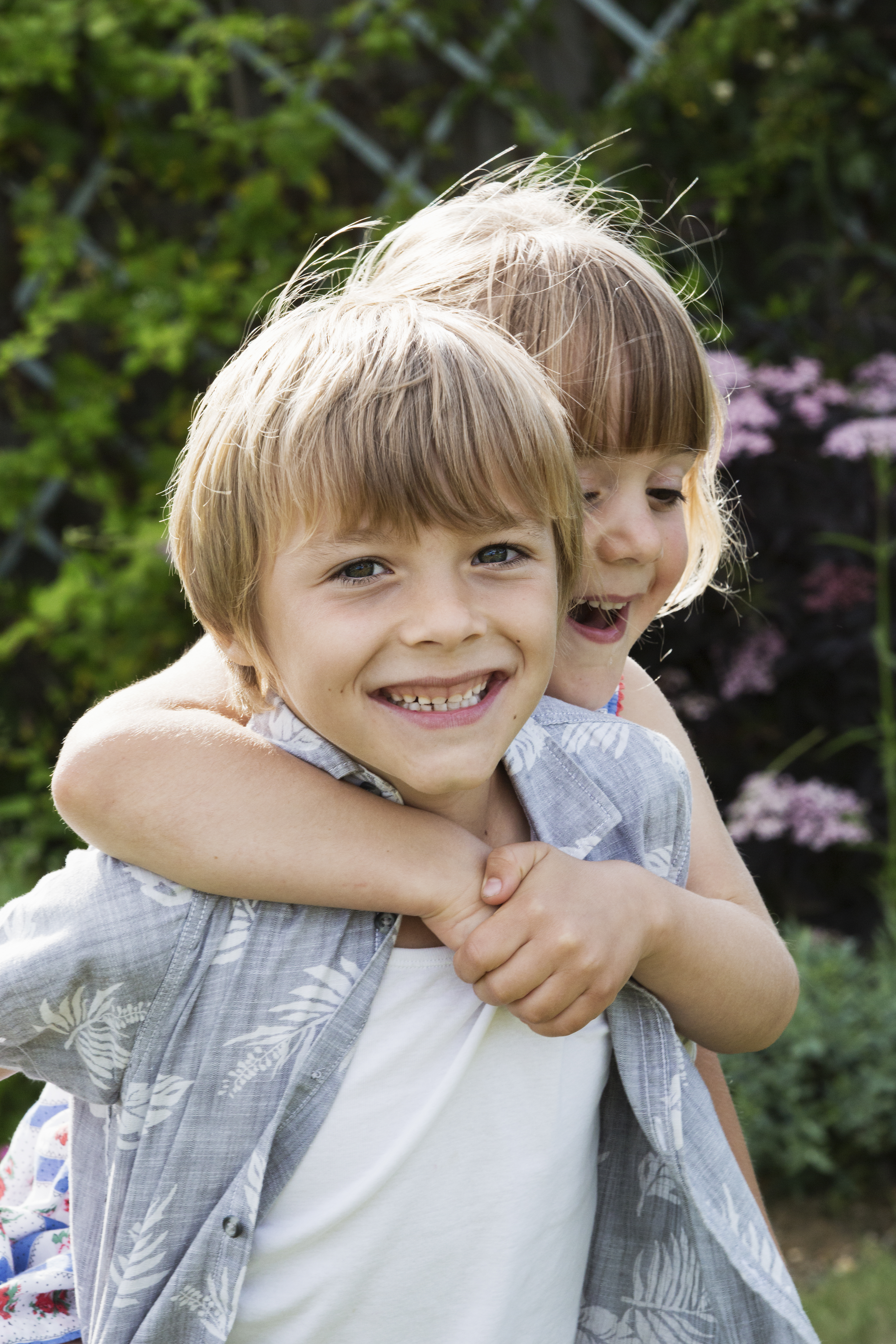 Girl hugging a smiling boy, looking at camera.
